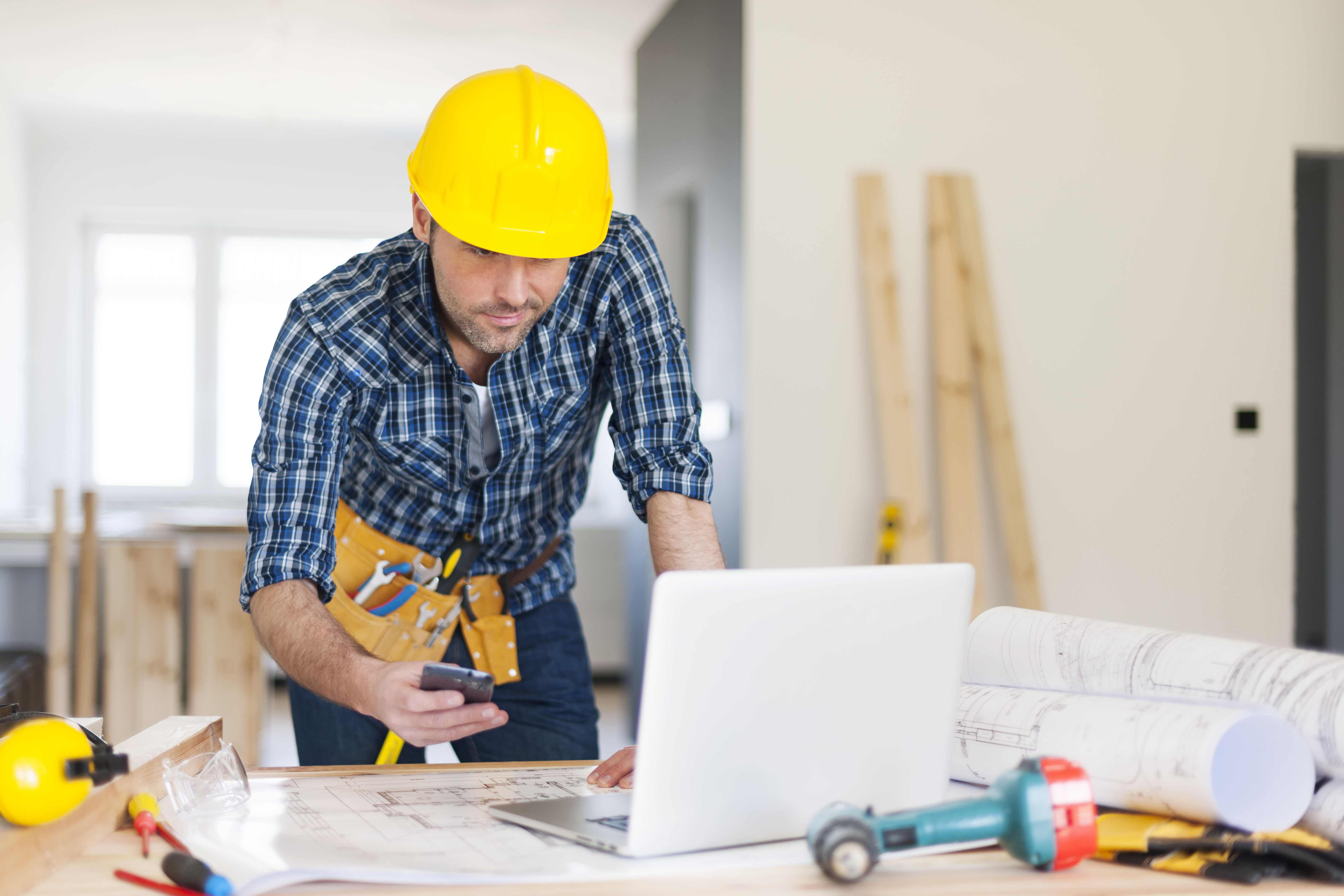Contractor reviewing blueprints on a laptop at a job site